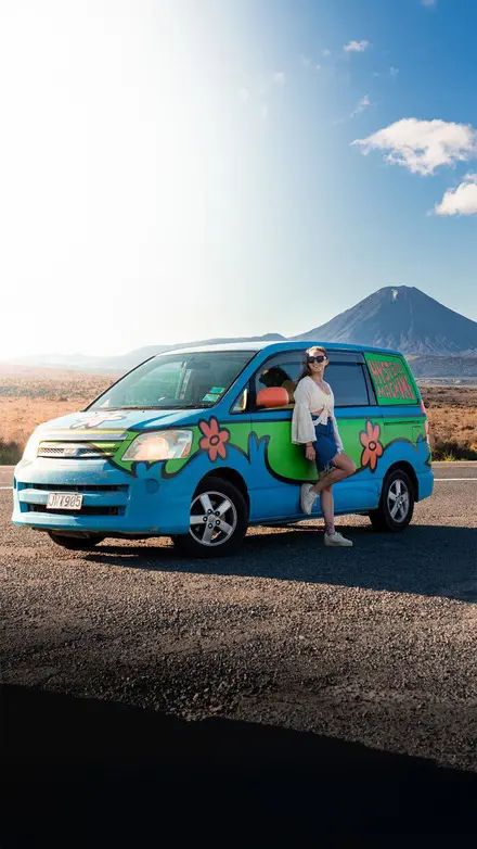 Traveller standing beside a colourful Mystery Machine van with Mount Tongariro in the background